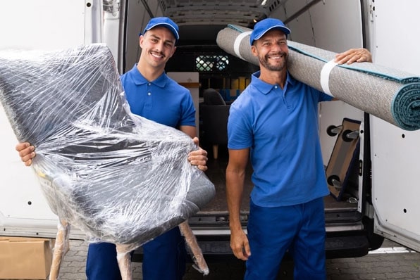 Entrümpelung Remscheid professionell und zuverlässig umgesetzt. Zwei Mitarbeiter von Entvita tragen bei einer Entrümpelung in Remscheid verpackte Möbel und einen Teppich aus einem Transporter.