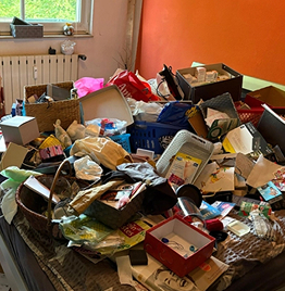 Messie-Entrümpelung in stark vermülltem Wohnzimmer mit Müllbergen auf Tisch und Boden