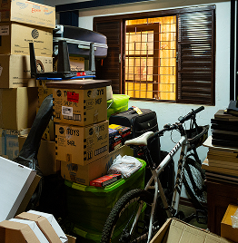 Wohnungsauflösung in überfülltem Raum mit Kartons, Fahrrad und gelagerten Haushaltsgegenständen