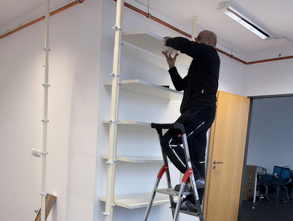 Regalböden-Abbau durch Entvita in Essen Mitarbeiter auf Leiter baut weiße Wandregale in einem Büroflur ab