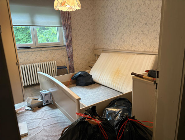 Festpreis-Entrümpelung – Schlafzimmerräumung Ausgebautes Bettgestell und schwarze Müllsäcke im Schlafzimmer