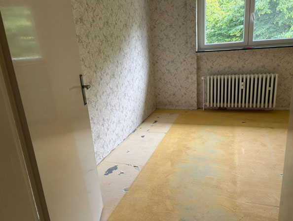 Festpreis Haushaltsauflösung Essen – leeres Zimmer Leergeräumtes Zimmer mit gelbem Boden und Radiator unter dem Fenster nach abgeschlossener Haushaltsauflösung